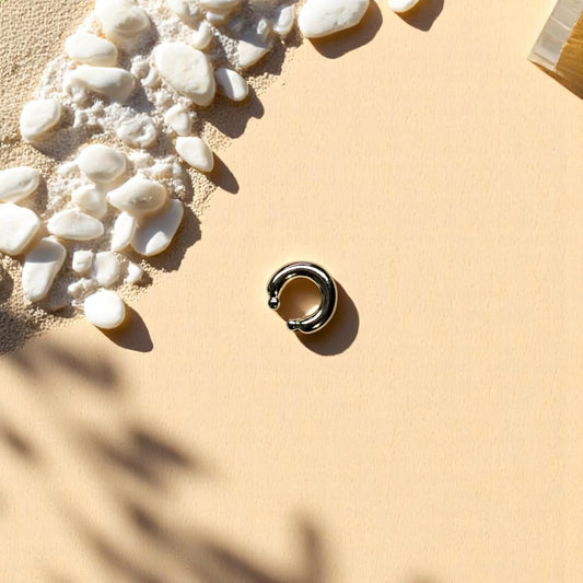 Earcuff dorado con extremos esféricos sobre fondo cuadriculado