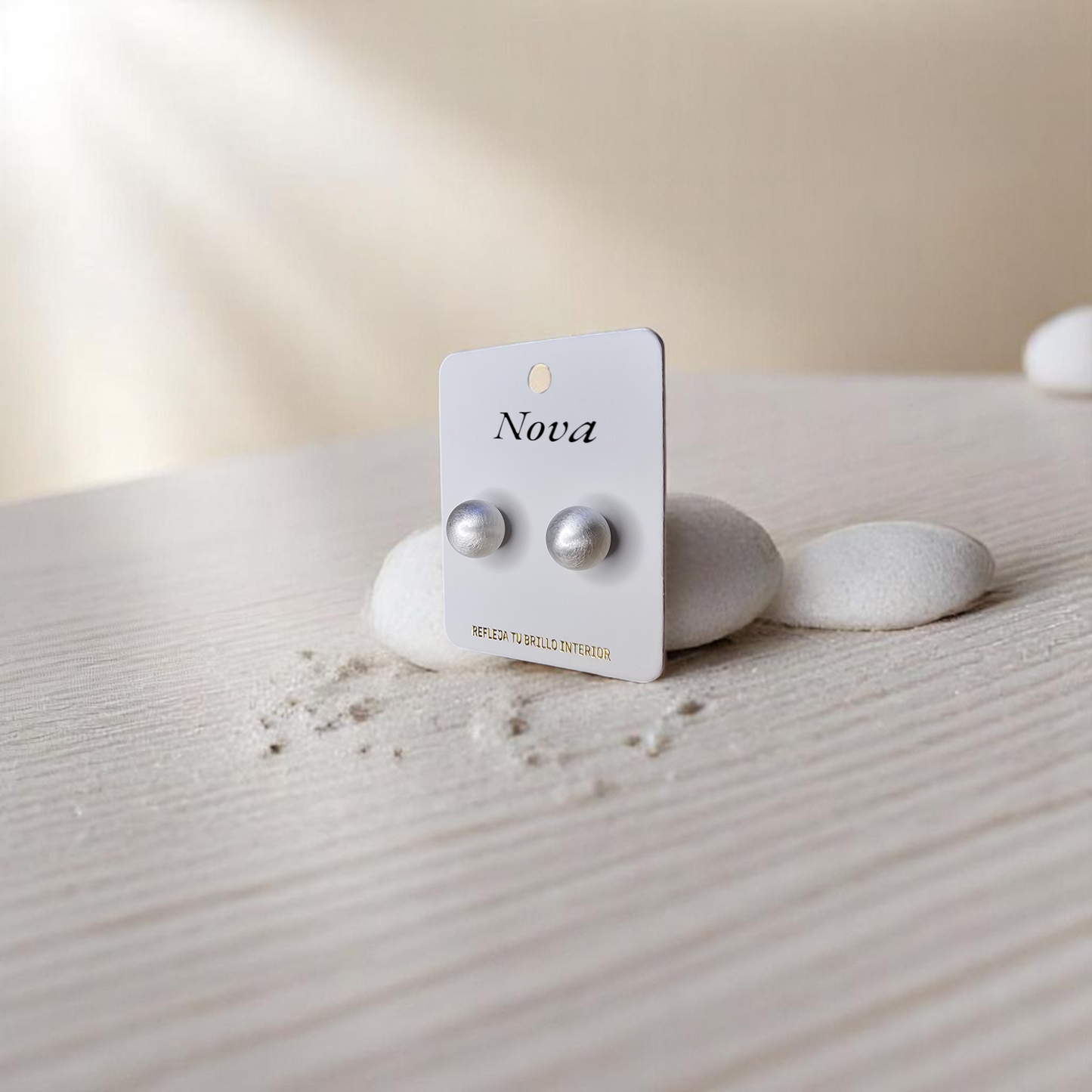 Aretes de bola mate Nova expuestos en escenario de arena clara