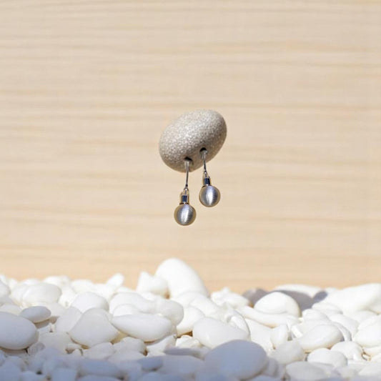 Aretes de bola mate Nova en metal hipoalergénico sobre fondo de piedras blancas