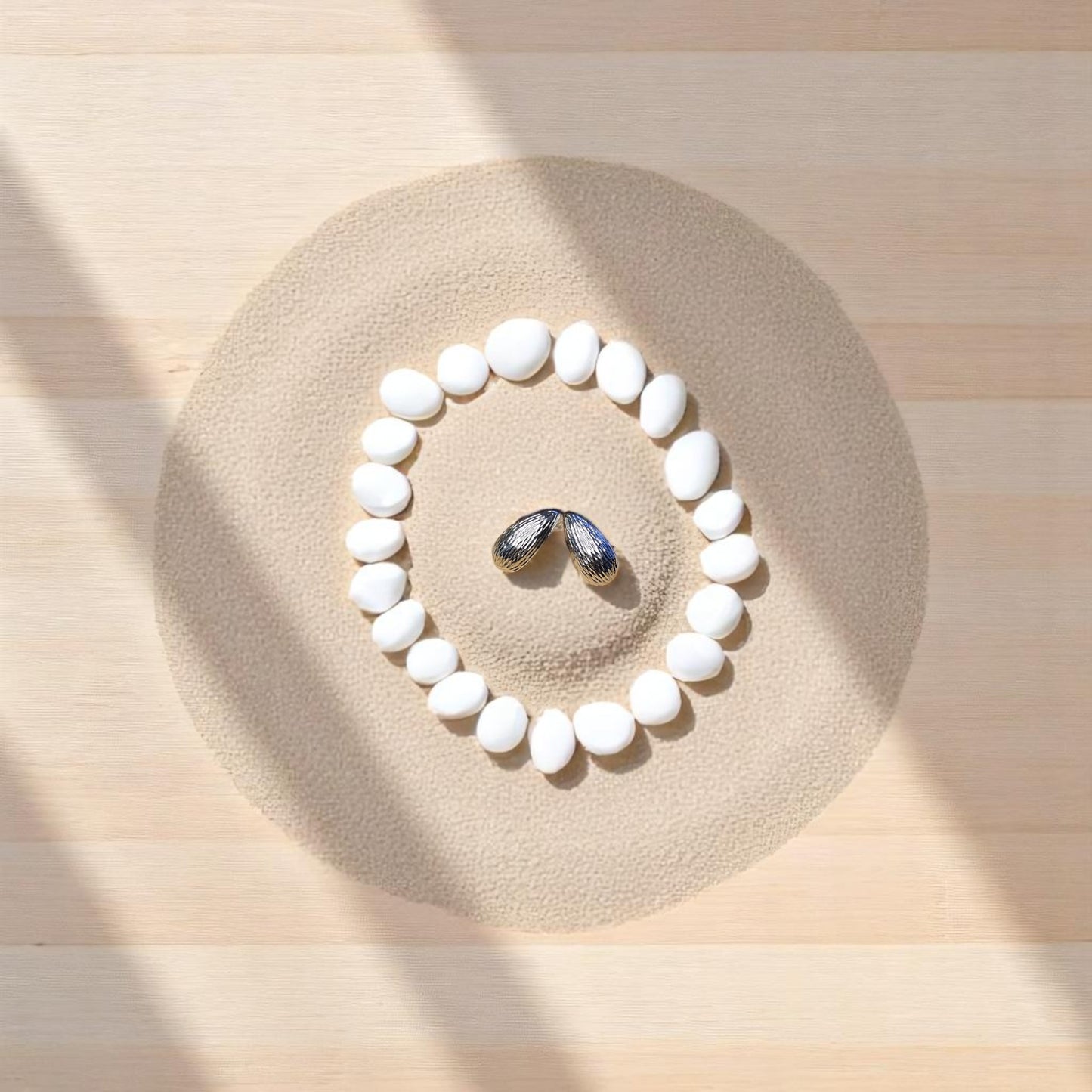 Aretes plateados sobre fondo de arena y piedras blancas