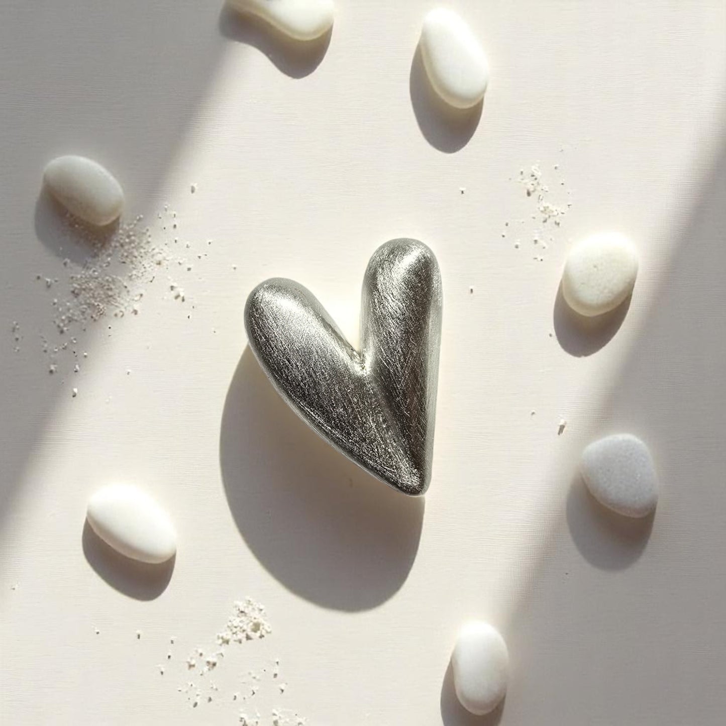 Aretes corazón en plata expuestos en arena con piedras blancas