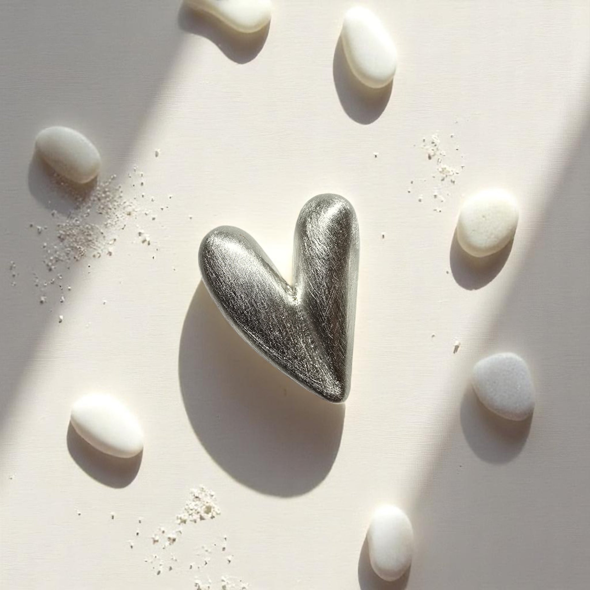 Aretes corazón en plata expuestos en arena con piedras blancas
