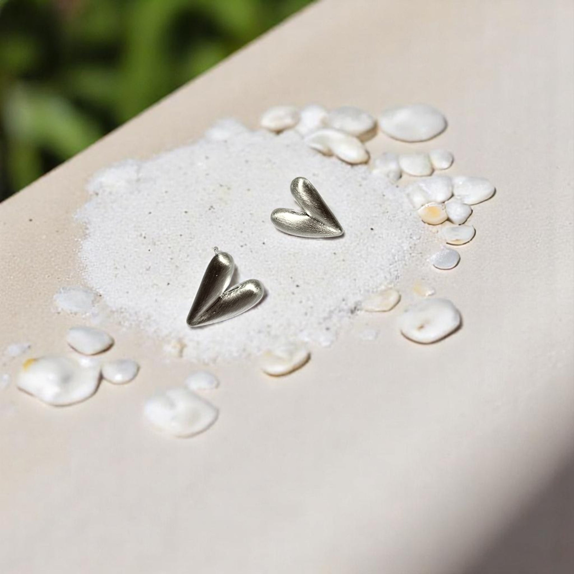 Aretes de plata en forma de corazón sobre arena blanca