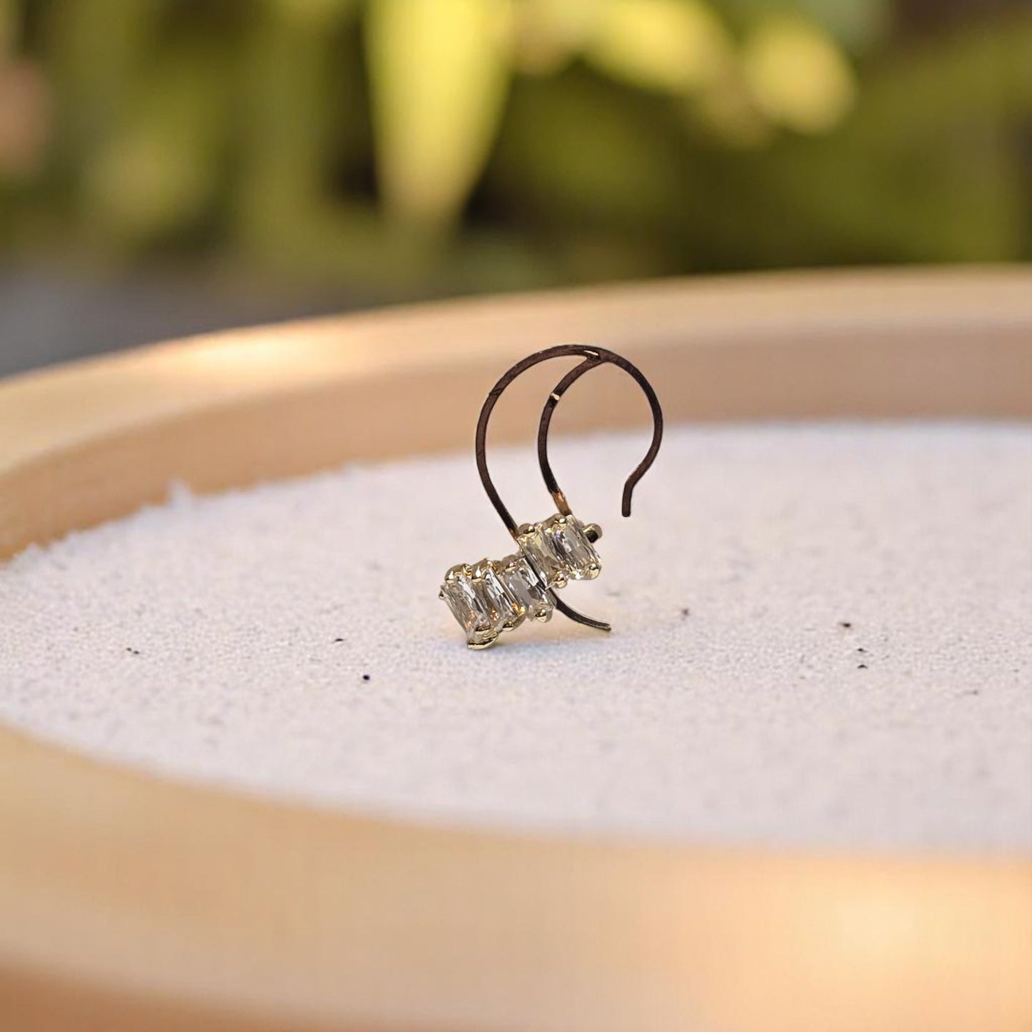 Earcuff de oro Nova con zirconias baguette sobre fondo de arena blanca