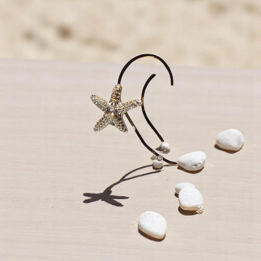 Earcuff de estrella de mar en plata con circonias brillando sobre arena blanca