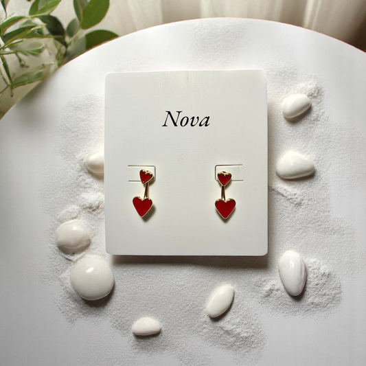 Par de aretes Nova con corazones rojos sobre superficie de madera clara