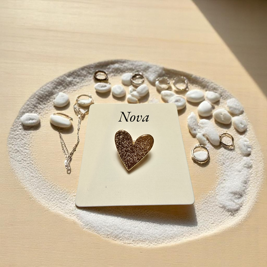 Anillo corazón dorado Nova sobre fondo claro y piedras blancas