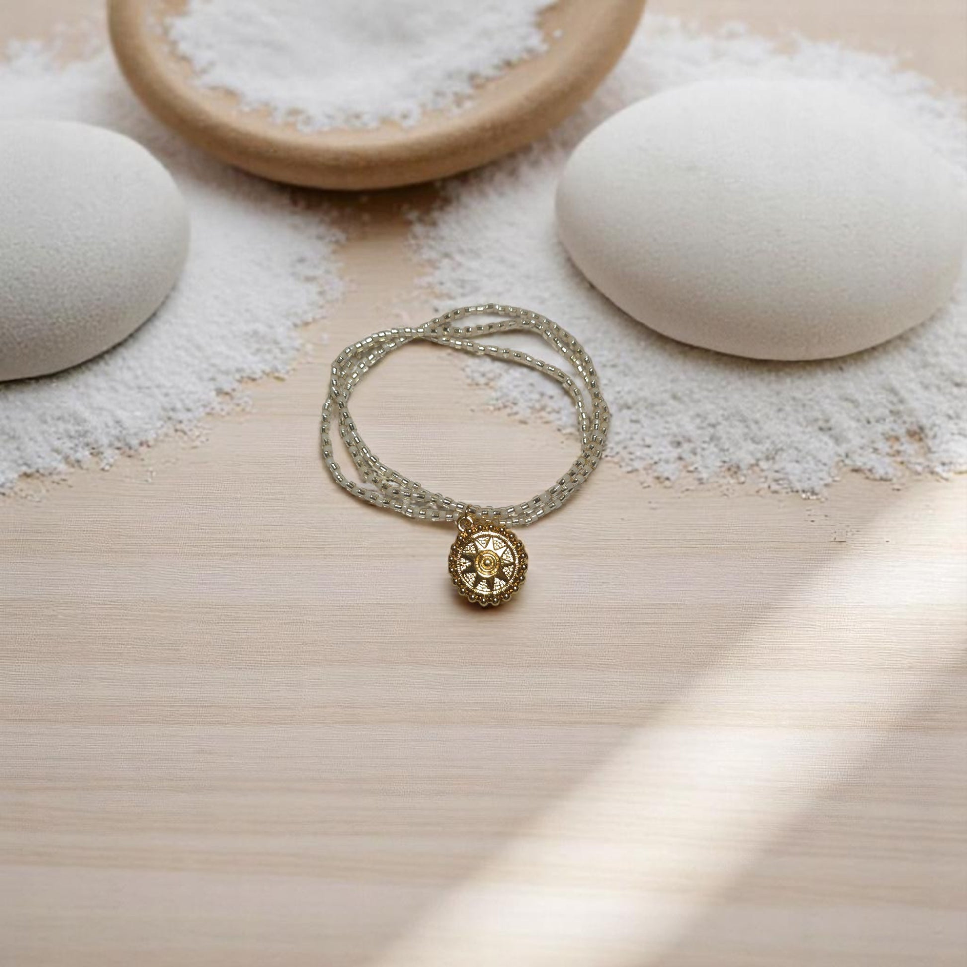 Pulsera triple con dije de sol sobre tabla de madera clara y elementos zen