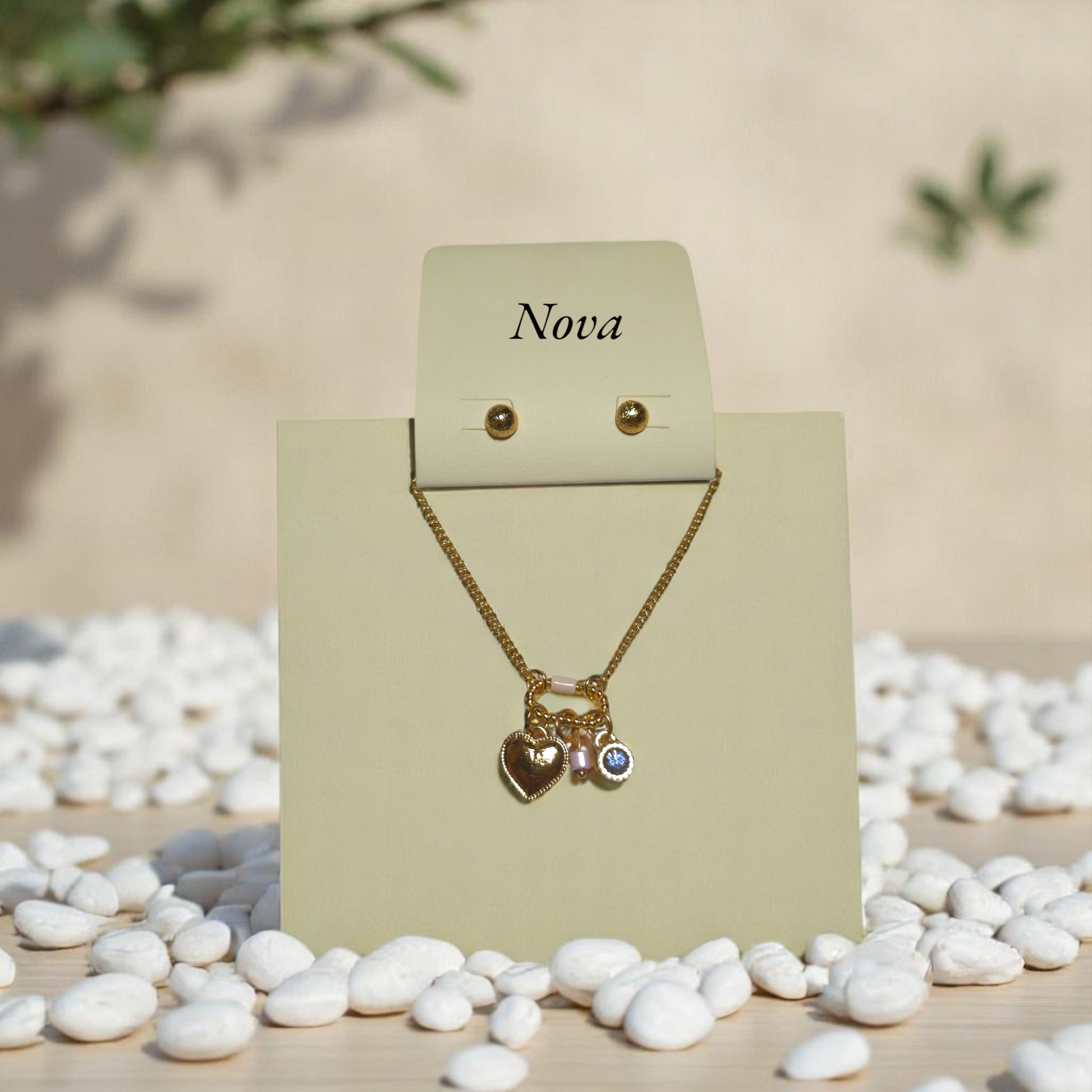 Set de pulsera dorada Nova con dijes de corazón y cristal azul sobre fondo de piedras blancas