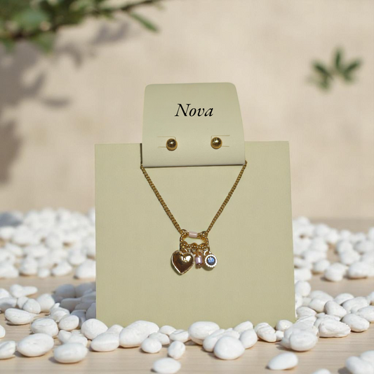 Set de pulsera dorada Nova con dijes de corazón y cristal azul sobre fondo de piedras blancas