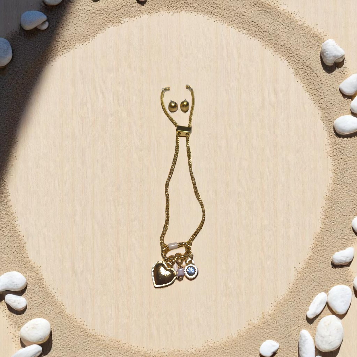 Set de pulsera dorada Nova con dijes de corazón y cristal azul sobre fondo de piedras blancas