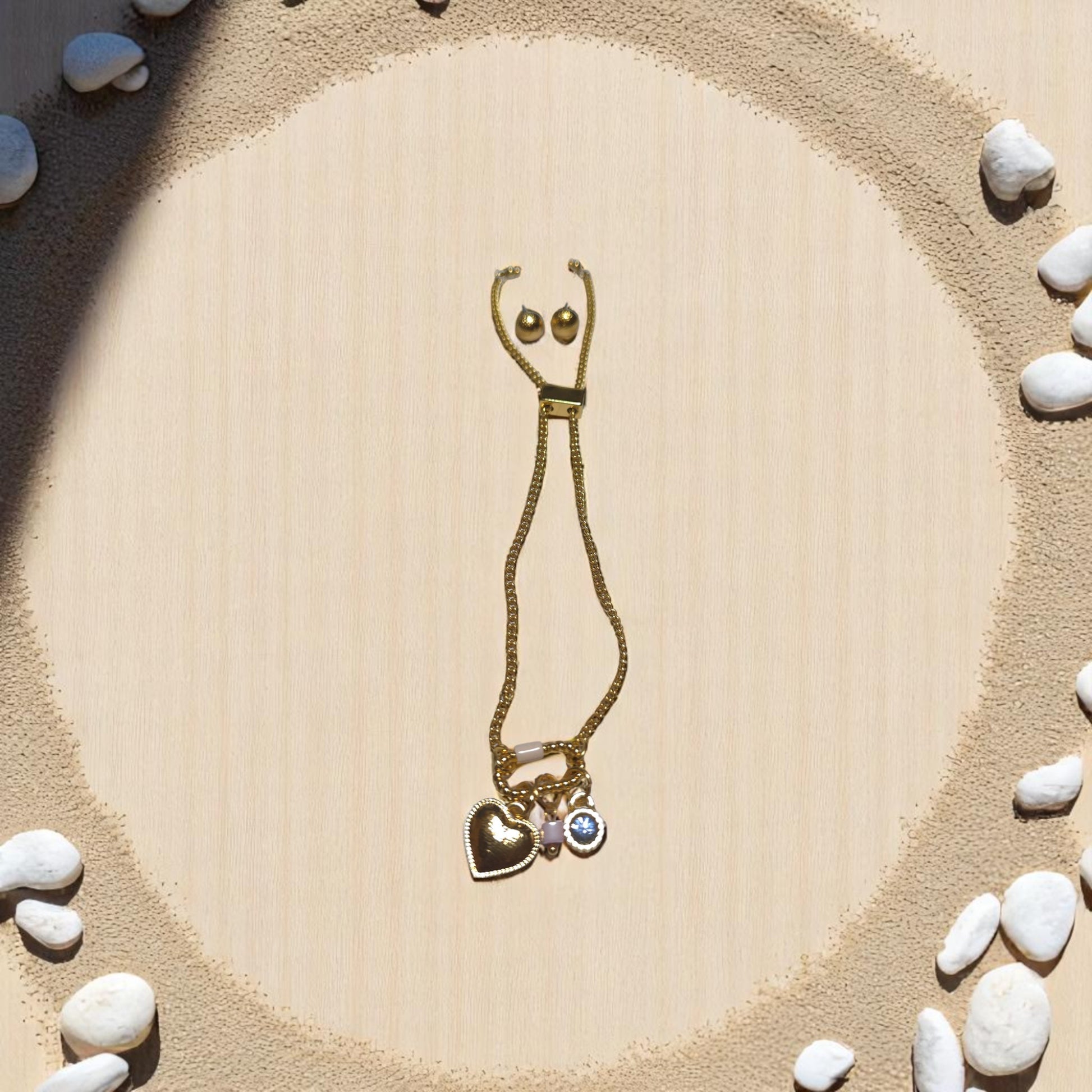 Set de pulsera dorada Nova con dijes de corazón y cristal azul sobre fondo de piedras blancas