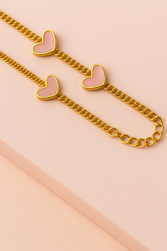Pulsera dorada con tres corazones rosa esmaltados sobre fondo oscuro