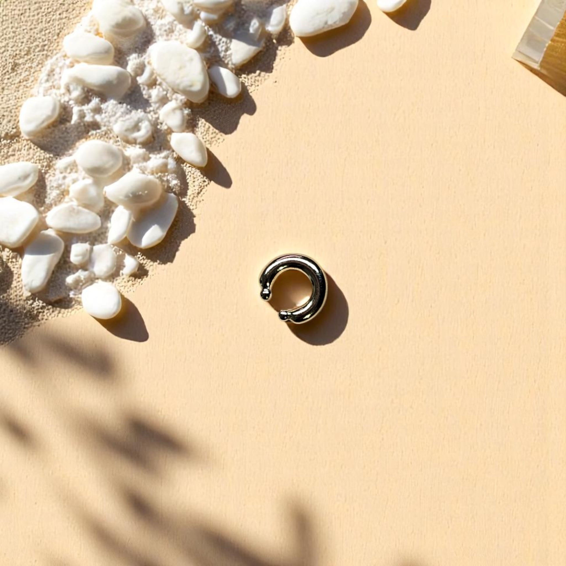 Earcuff dorado con extremos esféricos sobre fondo cuadriculado