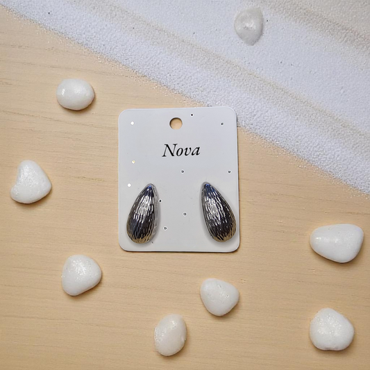 Aretes plateados sobre fondo de arena y piedras blancas